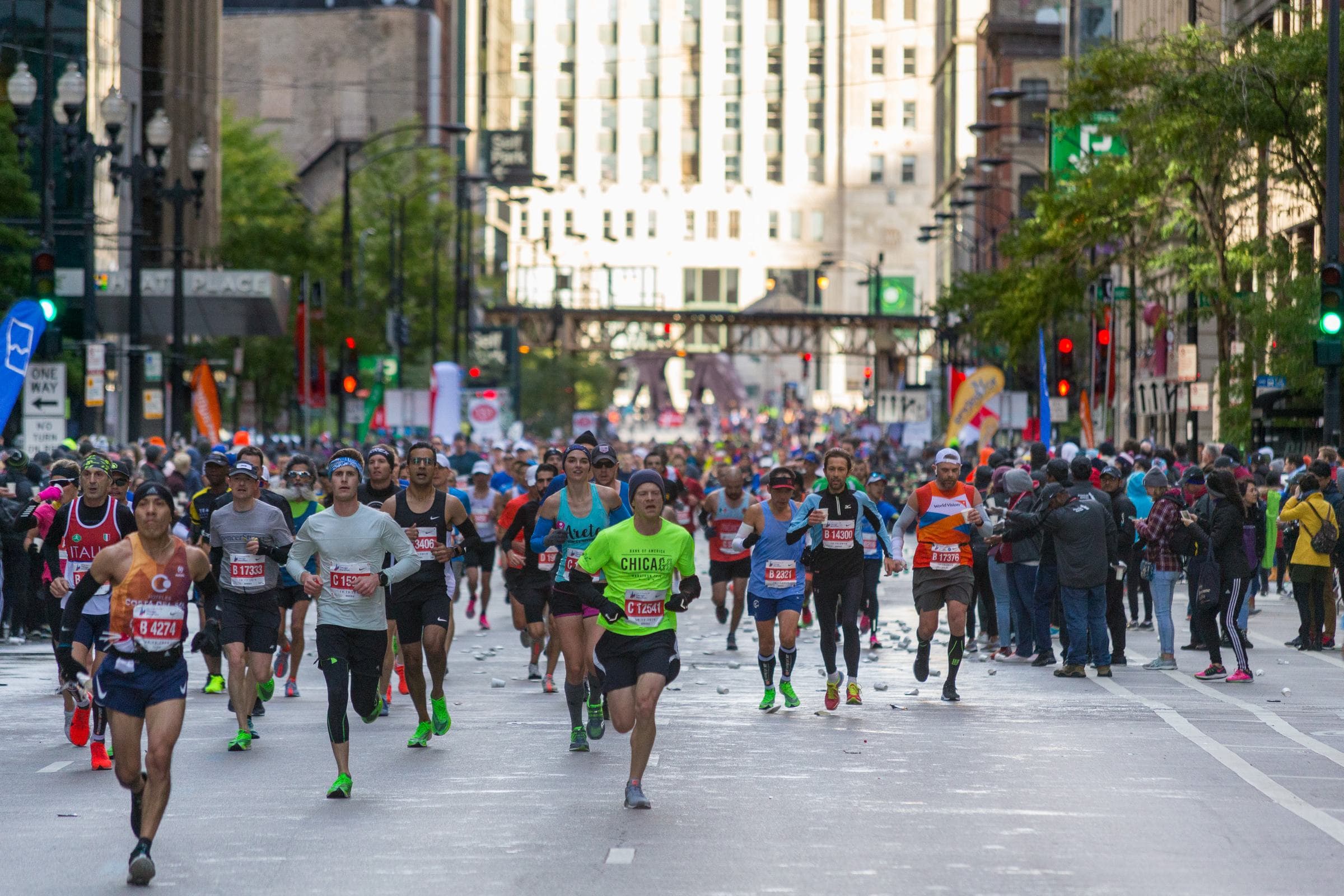 The mass field of the Chicago Marathon filling a downtown street beneath the L tracks